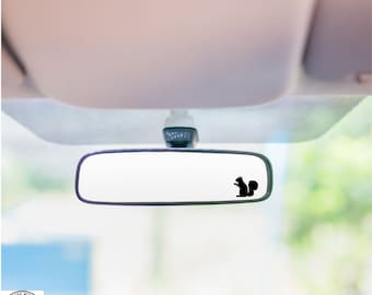 May include: A black silhouette of a squirrel is on the rearview mirror of a car. The mirror is reflecting a blurry image of the outside.