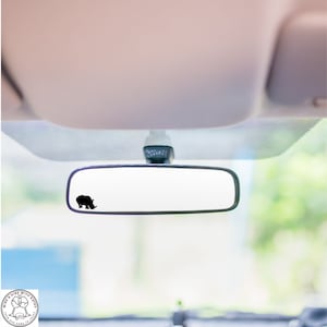 May include: A black rhinoceros silhouette sticker on a rearview mirror in a car.