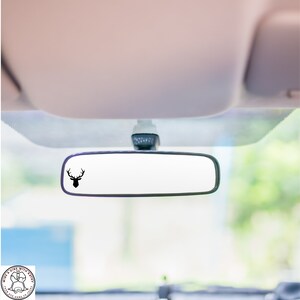 May include: A black silhouette of a deer head with antlers is on a rearview mirror in a car.
