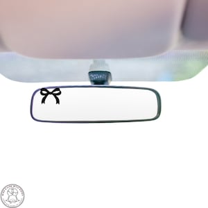 May include: A black bow sticker on a rearview mirror in a car.
