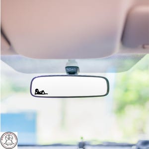 May include: A rearview mirror with a black silhouette of a person lying down on the glass.