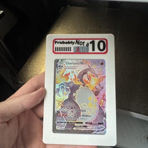 May include: A Charizard VMAX trading card encased in a white rectangular slab. The top of the slab features a red and black label with the text Probably Not a PANTO and the number 10. The card displays a holographic illustration of a dark dragon.