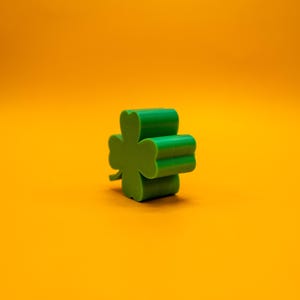 May include: A green four-leaf clover charm on a yellow background.