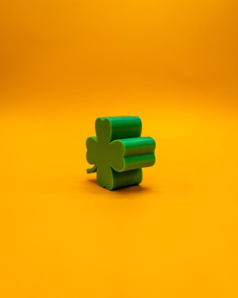 May include: A green four-leaf clover charm on a yellow background.