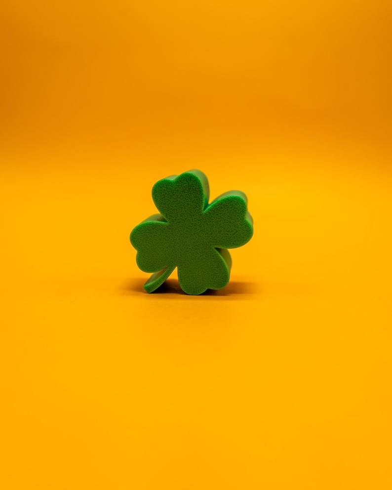 May include: A green four-leaf clover cutout on a bright orange background.