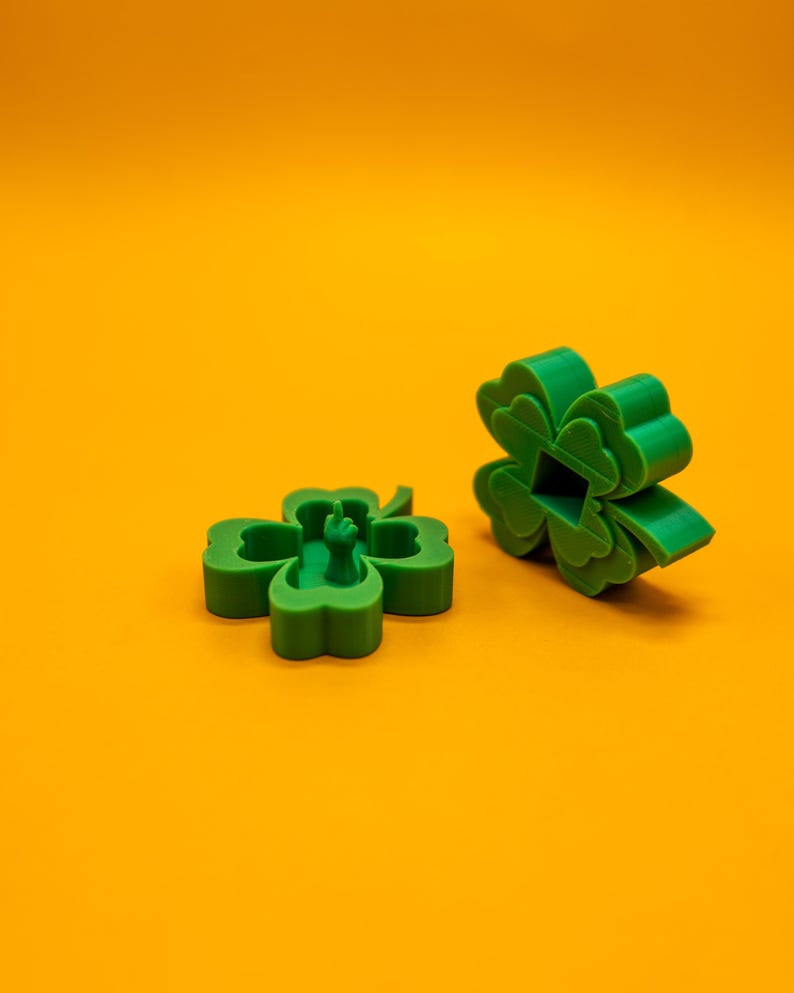 May include: Two green four-leaf clover shapes, one with a small green figure inside, on a solid orange background.