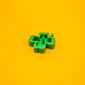 May include: A green four-leaf clover with a raised middle leaf, on a yellow background.