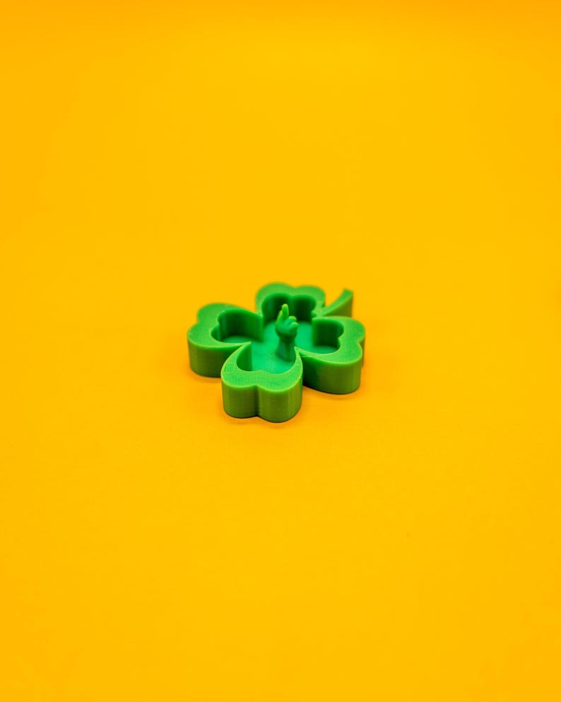 May include: A green four-leaf clover with a raised middle leaf, on a yellow background.