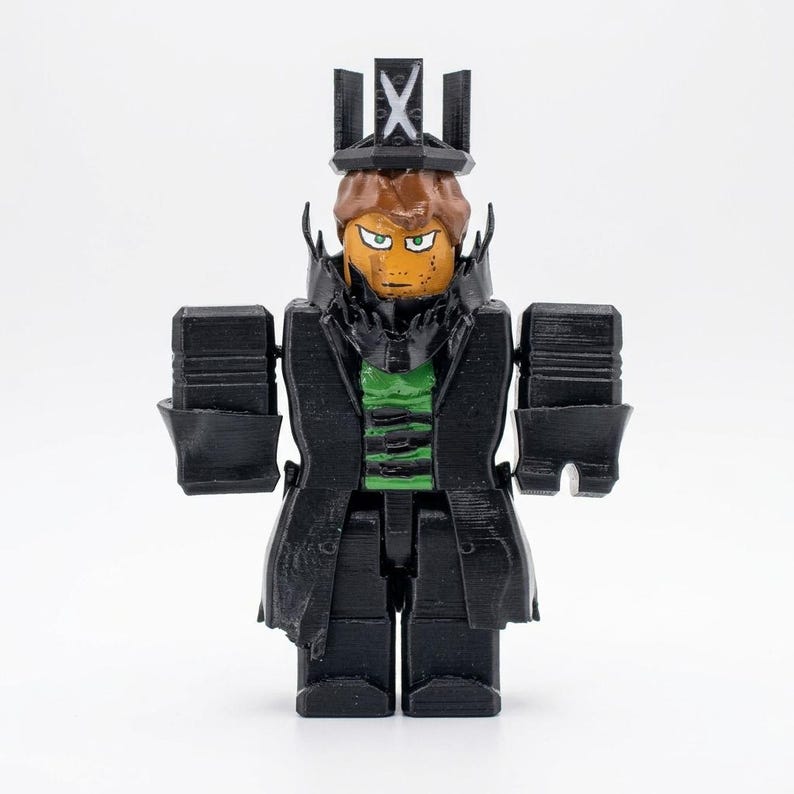 Puede incluir: Figura impresa en 3D de un personaje con abrigo negro, sombrero y rasgos cuadrados. La figura tiene una cara bronceada con ojos verdes y cabello casta&ntilde;o. Se ve una camisa verde debajo del abrigo. El sombrero tiene un dise&ntilde;o de cruz.