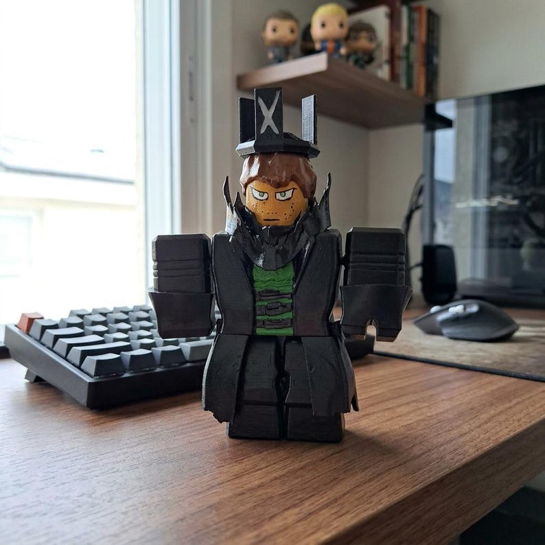 Puede incluir: Una figura de bloques negra y verde de un personaje con sombrero y abrigo. La figura tiene una cabeza marr&oacute;n con una expresi&oacute;n severa y una camisa verde. La figura est&aacute; de pie sobre un escritorio de madera cerca de un teclado y un rat&oacute;n de ordenador.