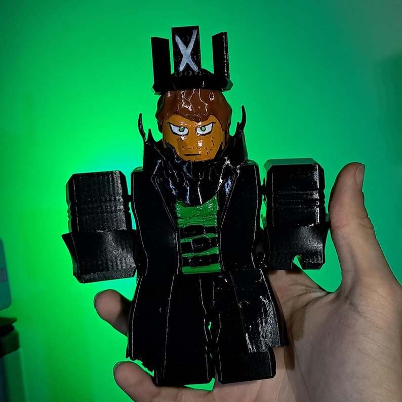 Puede incluir: Una figura impresa en 3D de un personaje con un abrigo negro, una camisa verde y una corona con una "X". La figura tiene una cara bronceada con ojos verdes y cabello casta&ntilde;o. El fondo es un degradado de verde.