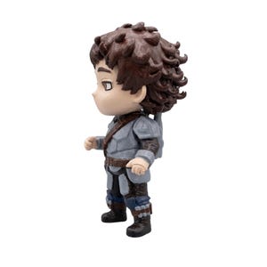 May include: A small figurine of a character with brown curly hair, wearing a gray tunic, brown belt, and dark blue pants. The figure has a small backpack and black boots. The figurine is standing on a white surface.