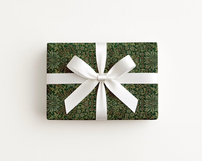A gift box with a green and white floral pattern and a white ribbon bow tied around it.