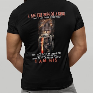 Pode incluir: Camiseta preta com um gr&aacute;fico de um le&atilde;o com uma espada e o texto "Eu sou o filho de um rei que n&atilde;o &eacute; movido pelo mundo. Porque o meu Deus est&aacute; comigo e vai &agrave; minha frente. N&atilde;o temo porque sou seu."