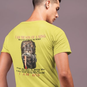 Pode incluir: Camiseta amarela com um gr&aacute;fico de um le&atilde;o preto e o texto "Eu sou o filho de um rei que n&atilde;o &eacute; movido pelo mundo" e "Porque o meu Deus est&aacute; comigo e vai &agrave; minha frente N&atilde;o temo porque sou seu".