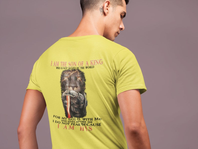 Pode incluir: Camiseta amarela com um gr&aacute;fico de um le&atilde;o preto e o texto "Eu sou o filho de um rei que n&atilde;o &eacute; movido pelo mundo" e "Porque o meu Deus est&aacute; comigo e vai &agrave; minha frente N&atilde;o temo porque sou seu".