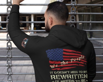 Puede incluir: Sudadera con capucha negra con un gráfico de bandera estadounidense desgastado y el texto "We The People It Doesn't Need To Be Rewritten It Needs To Be Reread".