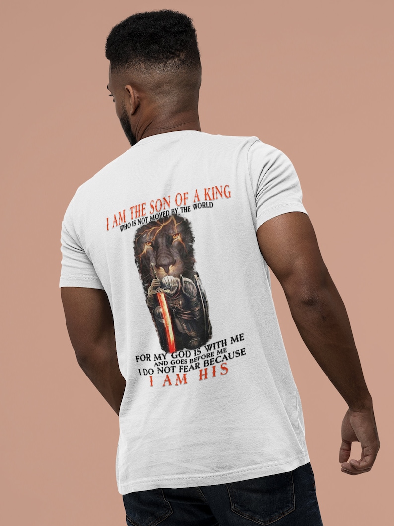 Pode incluir: Camiseta branca com um gr&aacute;fico de um le&atilde;o preto e o texto "Eu sou o filho de um rei que n&atilde;o &eacute; movido pelo mundo. Porque o meu Deus est&aacute; comigo e vai &agrave; minha frente. N&atilde;o temo porque sou seu."