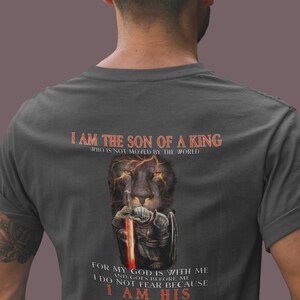 Pode incluir: Uma camiseta cinza escura com um gr&aacute;fico de le&atilde;o e o texto "Eu sou o filho de um rei que n&atilde;o &eacute; movido pelo mundo. Porque o meu Deus est&aacute; comigo e vai &agrave; minha frente. N&atilde;o temo porque sou seu."