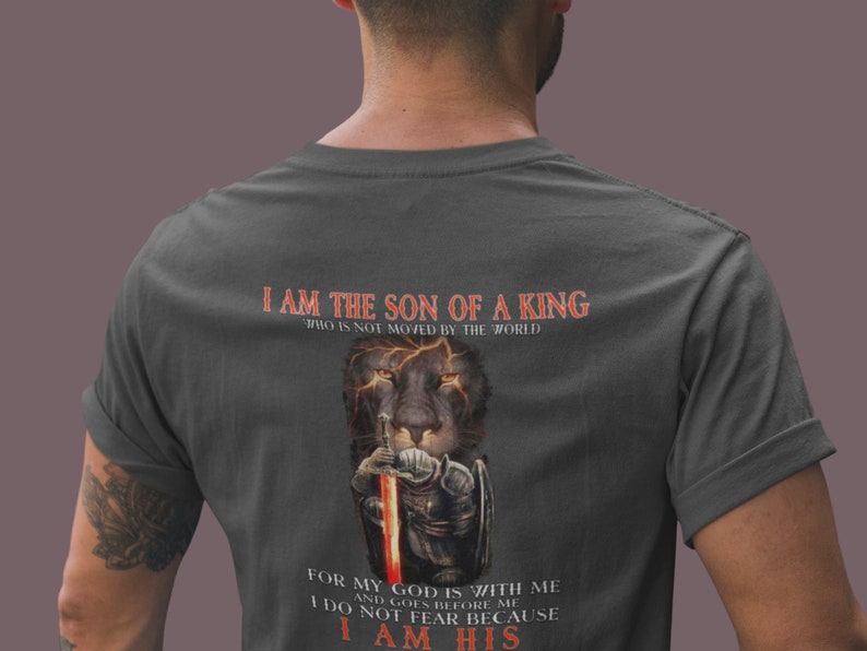 Pode incluir: Uma camiseta cinza escura com um gr&aacute;fico de le&atilde;o e o texto "Eu sou o filho de um rei que n&atilde;o &eacute; movido pelo mundo. Porque o meu Deus est&aacute; comigo e vai &agrave; minha frente. N&atilde;o temo porque sou seu."