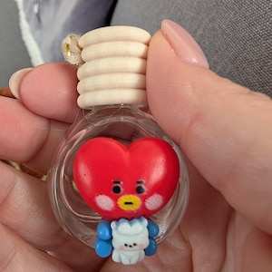 May include: A clear glass bottle with a wooden cap and a red heart-shaped character inside. The character has a yellow beak, black eyes, and blue arms. A small white character is attached to the bottom of the red heart.