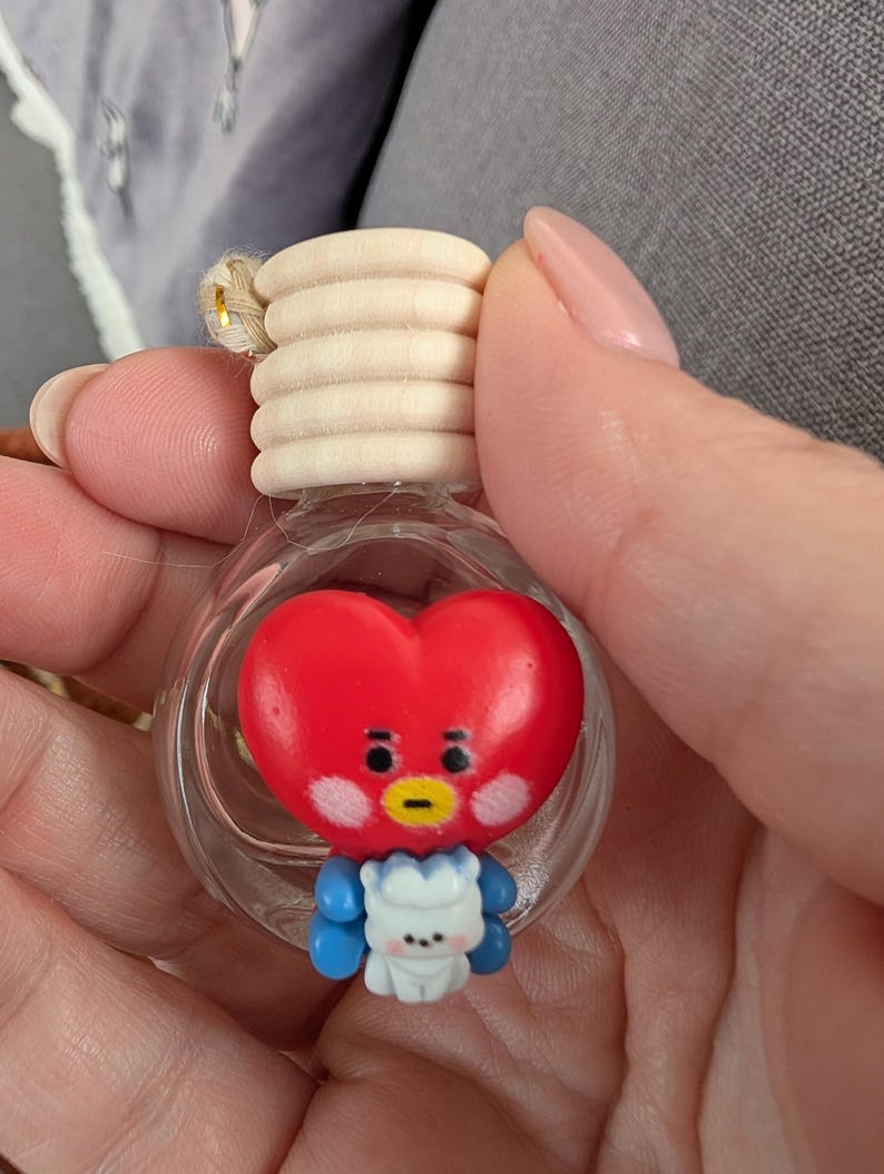 May include: A clear glass bottle with a wooden cap and a red heart-shaped character inside. The character has a yellow beak, black eyes, and blue arms. A small white character is attached to the bottom of the red heart.