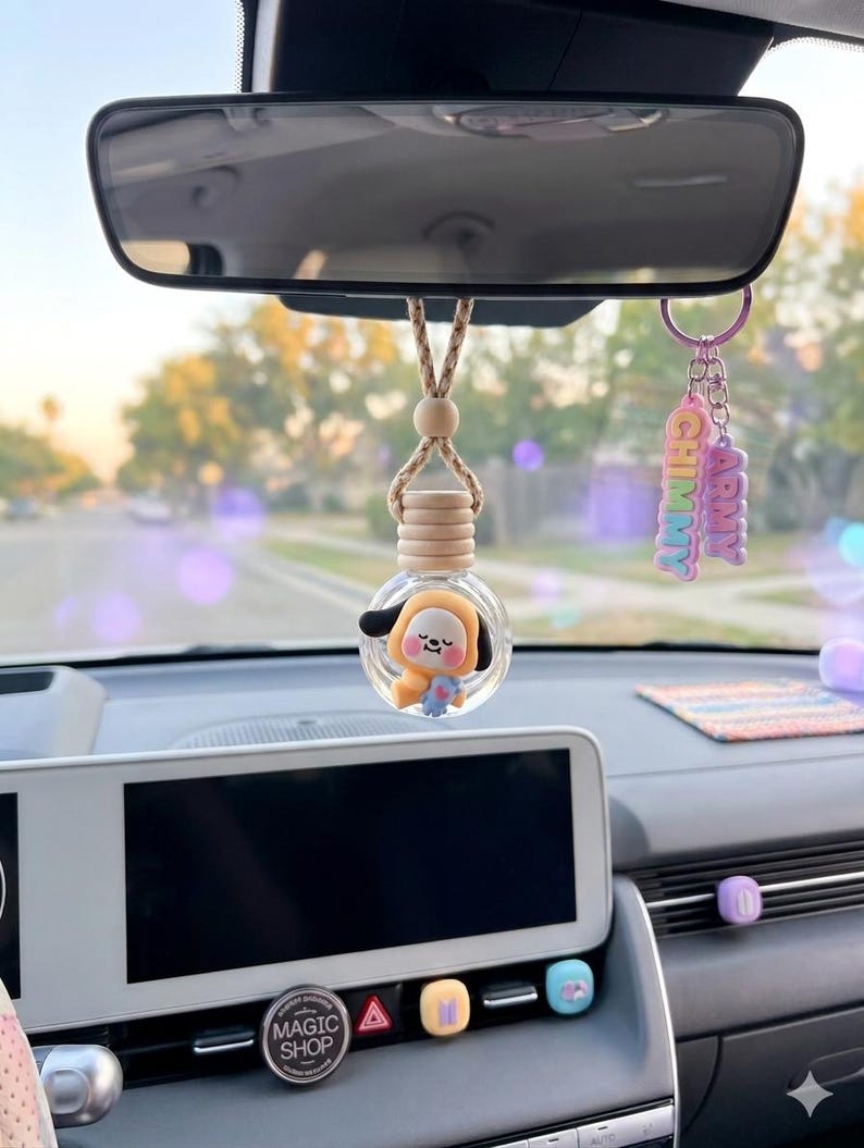 May include: A car interior featuring a hanging air freshener with a cartoon character inside a glass bottle. A keychain with the text "CHIMMY ARMY" hangs nearby. The car's dashboard includes a "MAGIC SHOP" button.