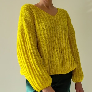 May include: A bright yellow knitted jumper with a v-neck and long sleeves. The jumper has a ribbed texture and a loose fit.
