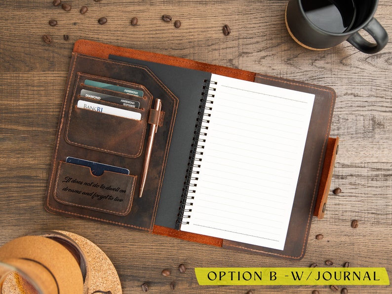 May include: Open leather journal with a spiral-bound notebook and card slots. A rose gold pen rests in a loop. The journal has the quote "It does not do to dwell on dreams and forget to live." A black mug of coffee sits nearby.