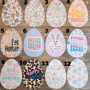 May include: Twelve colorful Easter egg designs featuring various patterns and text, including "Egg Hunter", "Happy Easter", and "Don't Worry Be Hoppy".