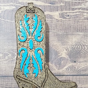 May include: A decorative cowboy boot made of metal with a turquoise blue design. The boot is a light gold color and has a textured surface.