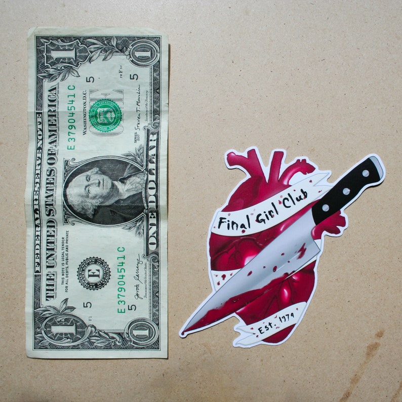 May include: A red heart with a knife through it. The heart has a white banner that says "Final Girl Club" and "Est. 1979".