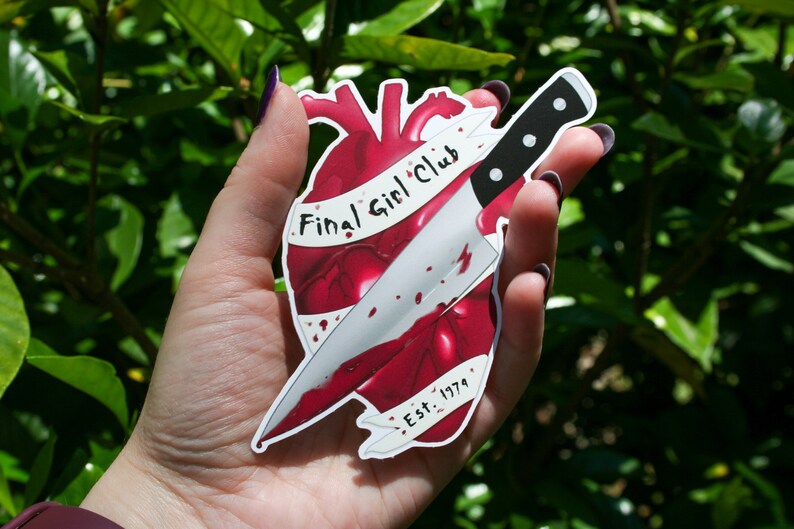 May include: A red heart with a knife through it, with the text "Final Girl Club Est. 1979" on a white banner.