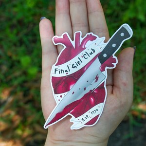 May include: A sticker of a red heart with a knife through it. The heart has the text "Final Girl Club" and "Est. 1979" on it.