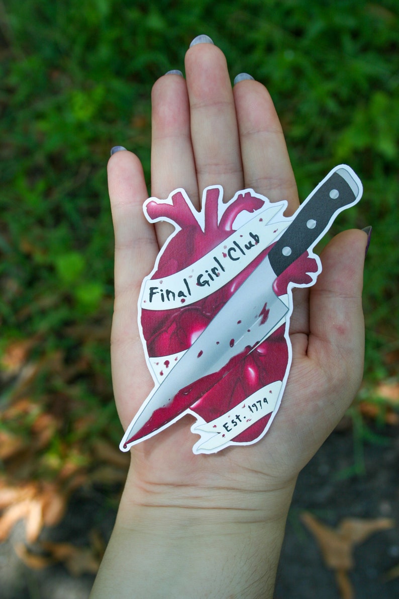 May include: A sticker of a red heart with a knife through it. The heart has the text "Final Girl Club" and "Est. 1979" on it.