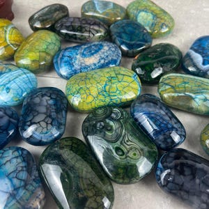 May include: A collection of polished dragon vein agate stones in various colors, including blue, green, and yellow. The stones have unique crackle patterns and are oval-shaped.