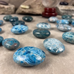 May include: A collection of polished, oval-shaped gemstones in shades of blue and teal. The stones have a mottled appearance with varying patterns and textures. Some stones are a vibrant turquoise, while others are a deeper teal.