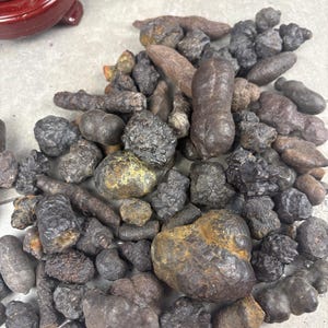 May include: A collection of dark, metallic-looking mineral nodules and concretions with irregular, bumpy, and rounded shapes. The stones exhibit a mix of charcoal, brown, and bronze-toned surfaces with varying textures, ranging from smooth to rough.