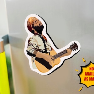 K&ouml;nnte beinhalten: Ein Aufkleber mit einer stilisierten Illustration einer Person, die eine Akustikgitarre spielt. Die Person tr&auml;gt einen Turban und ein gemustertes Hemd. Der Aufkleber hat einen wei&szlig;en Rand und den Text "NOW AVAILABLE AS MAGNET" in einer gelben Sprechblase.