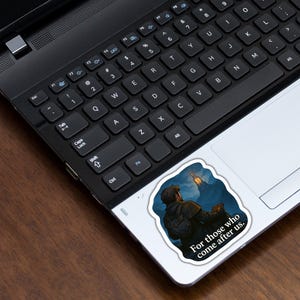 May include: A sticker featuring a detailed illustration of a person looking up at a glowing structure against a dark, cloudy sky. The sticker has the text "For those who come after us." The sticker is on a laptop.