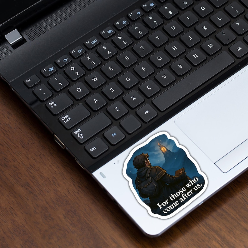 May include: A sticker featuring a detailed illustration of a person looking up at a glowing structure against a dark, cloudy sky. The sticker has the text "For those who come after us." The sticker is on a laptop.