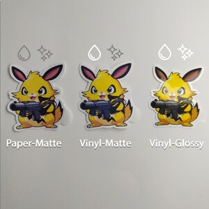 May include: Three stickers featuring a yellow cartoon character with a gun. The stickers are labeled "Paper-Matte", "Vinyl-Matte", and "Vinyl-Glossy". Each sticker has a white border and is on a white background.