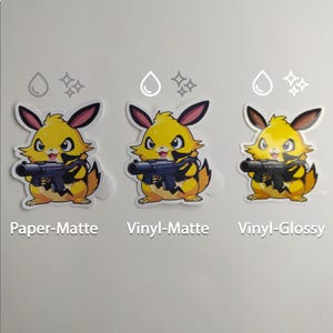 Pode incluir: Tr&ecirc;s autocolantes com uma personagem de desenho animado amarela segurando uma arma. Os autocolantes est&atilde;o rotulados como "Paper-Matte", "Vinyl-Matte" e "Vinyl-Glossy". Cada autocolante tem uma borda branca.
