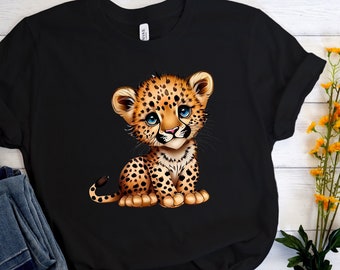 Può includere: Maglietta nera con un'immagine di un cucciolo di leopardo cartone animato con occhi blu. Il leopardo è seduto sulle zampe posteriori con le zampe anteriori davanti a lui.