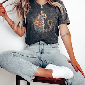 May include: A dark grey t-shirt featuring a colourful floral cat design. The cat is looking to the right and has a light brown and white coat. The flowers are in shades of pink, yellow, orange, and green.