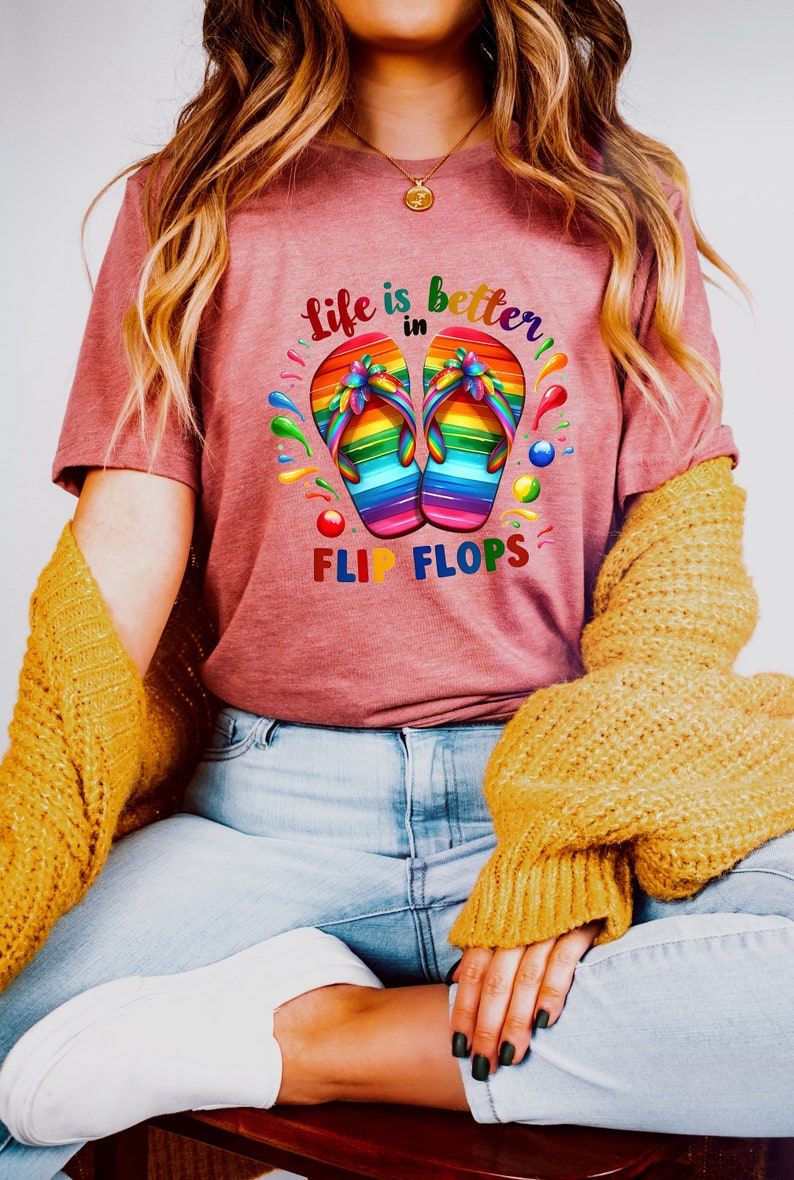 May include: A maroon t-shirt with the text "Life is better in Flip Flops." The shirt features a colorful graphic of rainbow-colored flip-flops. The shirt is paired with light blue jeans and a yellow sweater.