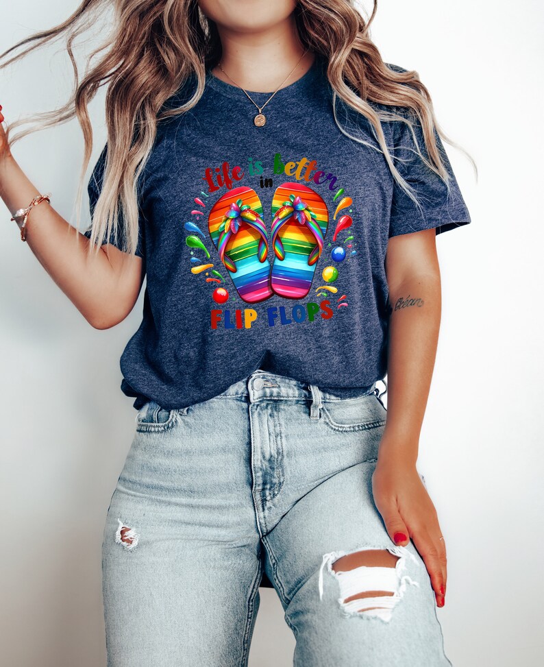 May include: Navy blue t-shirt with the text "Life is better in Flip Flops." The shirt features a colorful graphic of rainbow-colored flip-flops. The design includes splashes of color around the flip-flops, creating a vibrant and summery feel.