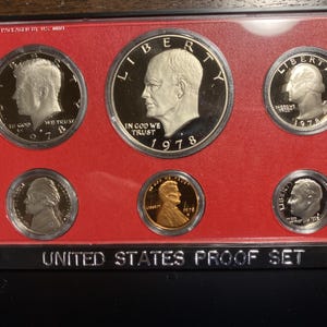Könnte beinhalten: Ein US-Proof-Set aus dem Jahr 1978. Das Set enthält einen halben Dollar, einen Viertel-Dollar, einen Dime, einen Nickel und einen Penny. Die Münzen sind in einem schwarzen und roten Etui angeordnet, auf dem vorne "United States Proof Set" steht.