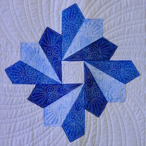 Op de afbeelding: Een blauw en wit quilt met een draaiend patroon in het midden. De quilt is gemaakt van stof met een bloemenpatroon.