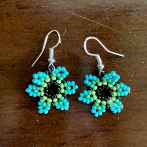 May include: A pair of beaded earrings with a flower design. The earrings are made with black, green, and blue beads. The earrings have silver hooks.